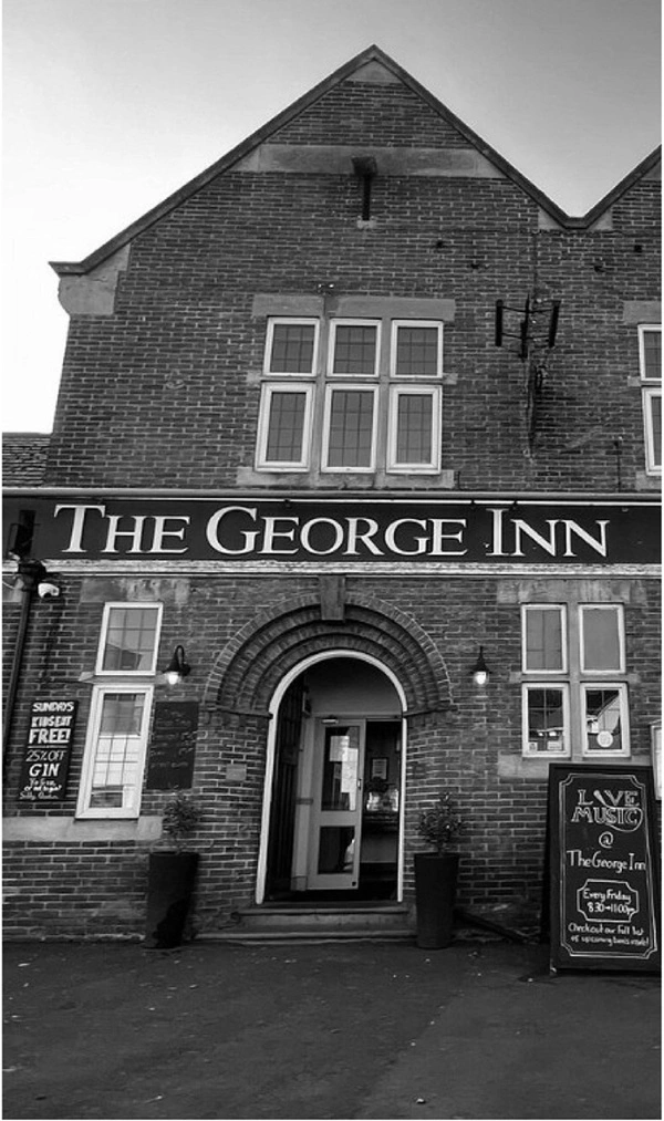 A Black and White Photograph of the front of the George Inn, Showing the George Inn from pavement side in a central village location, a typical victorian period property with red brick